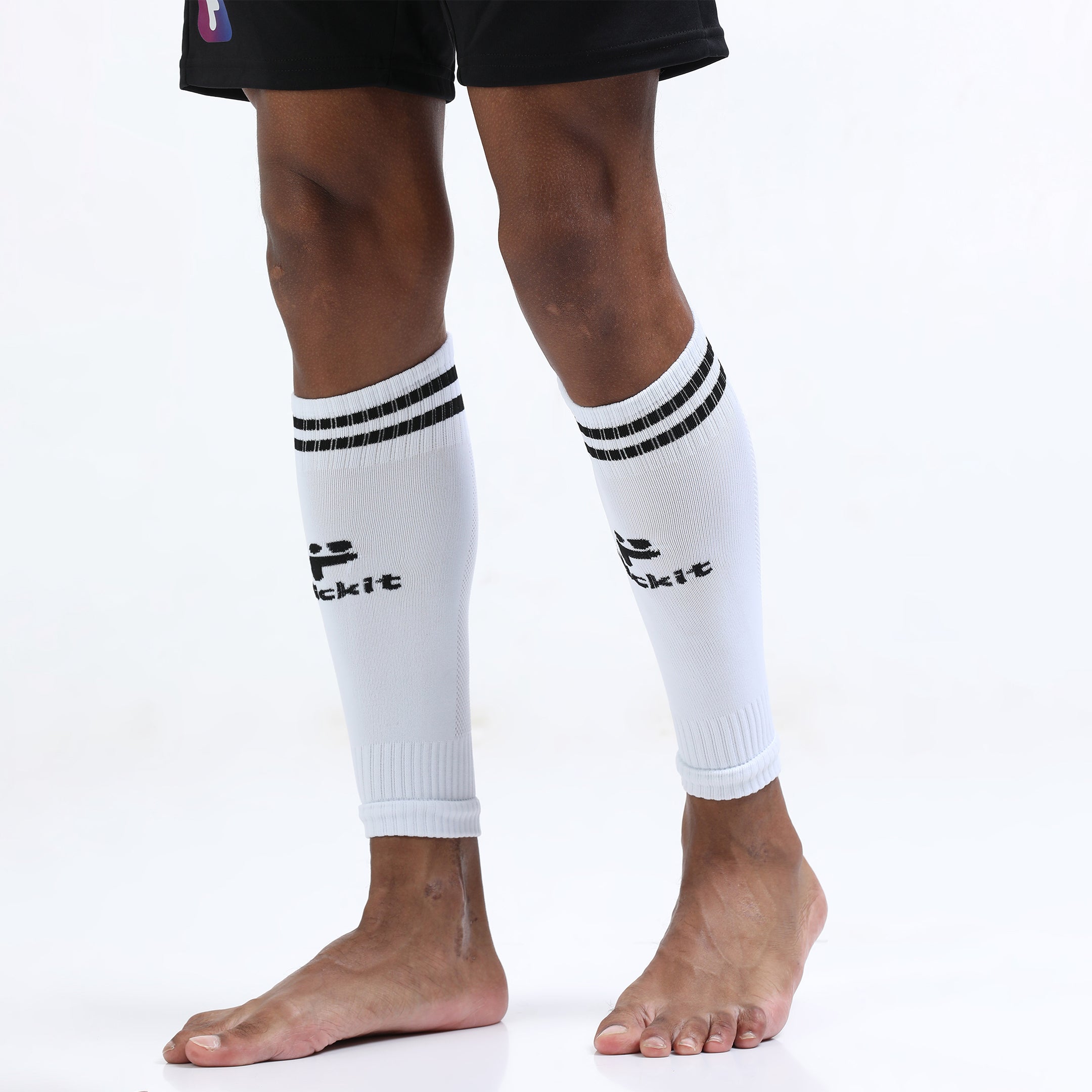 White leg warmers with black stripes and 'kickit' branding worn by a person on a white background