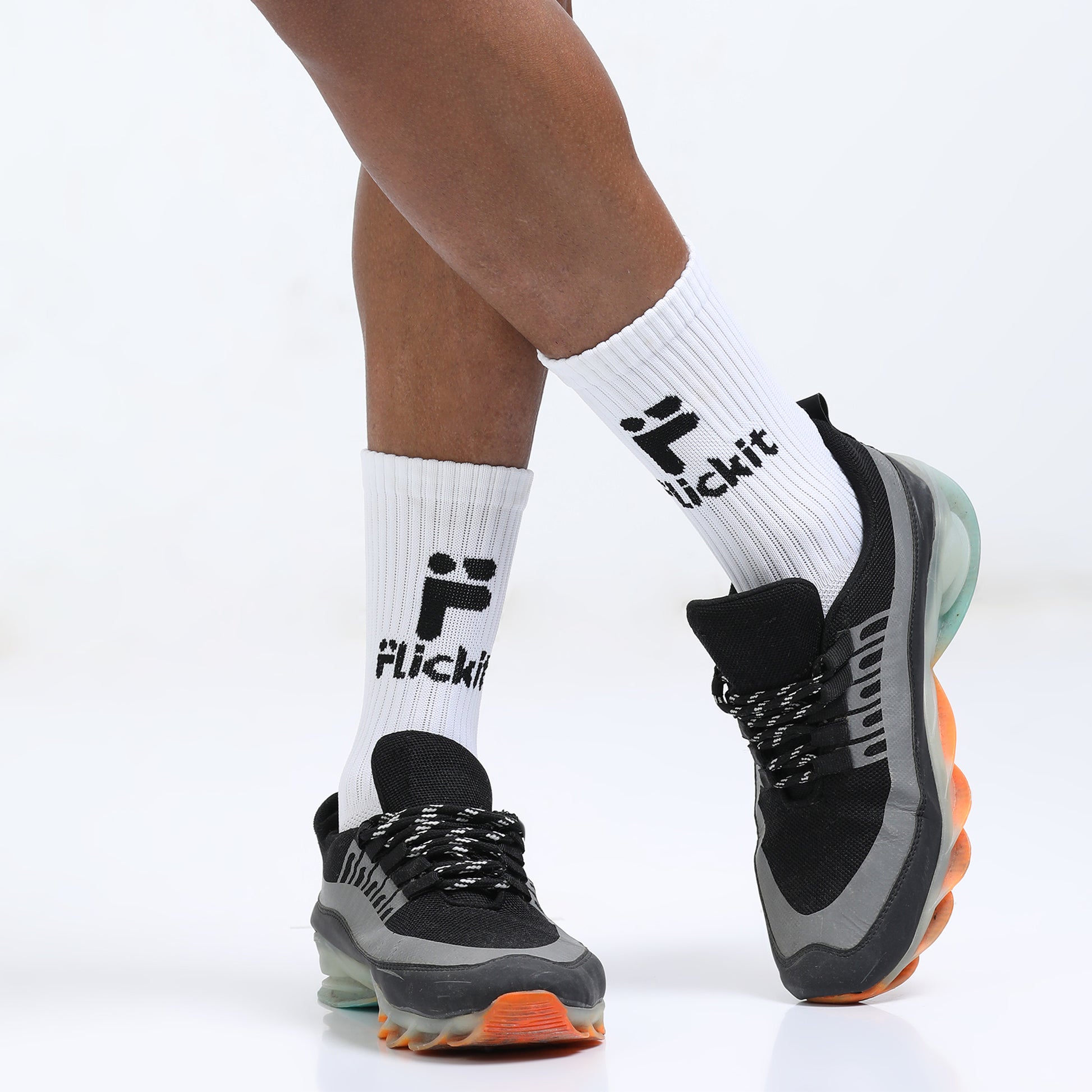 Black and gray sneakers with orange sole worn with white socks featuring a logo on a white background