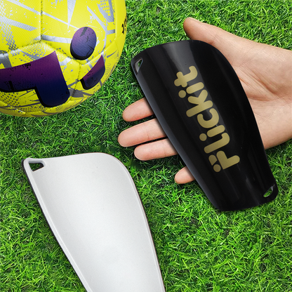 Person holding a black 'flickit' container on grass with a soccer ball in the background