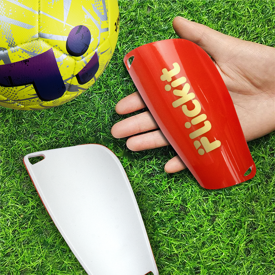 Red shin guard with 'Flickit' branding on grass next to a soccer ball